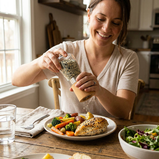 Femme utilisant le Sel au Sésame & Sapin Baumier des Épices du Guerrier dans un moulin sur un repas de poulet et légumes